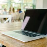 Laptop auf Holz Tisch in einem hellen Raum mit Menschen im Hintergrund.