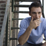 Mann raucht auf einer metallenen Außentreppe.