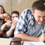 Trauriger Mann, andere lachen im Hintergrund.