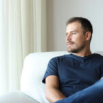 Mann schaut aus dem Fenster, nachdenklich auf Sofa.