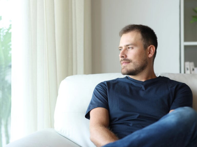 Mann schaut aus dem Fenster, nachdenklich auf Sofa.