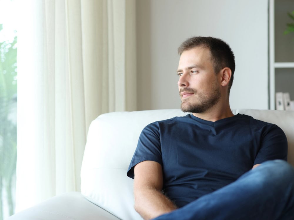 Mann schaut aus dem Fenster, nachdenklich auf Sofa.